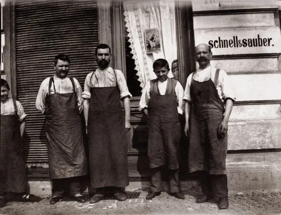 Vier Berliner Handwerker in Schürzen vor ihrer Werkstatt, auf der Scheibe steht schnell und sauber