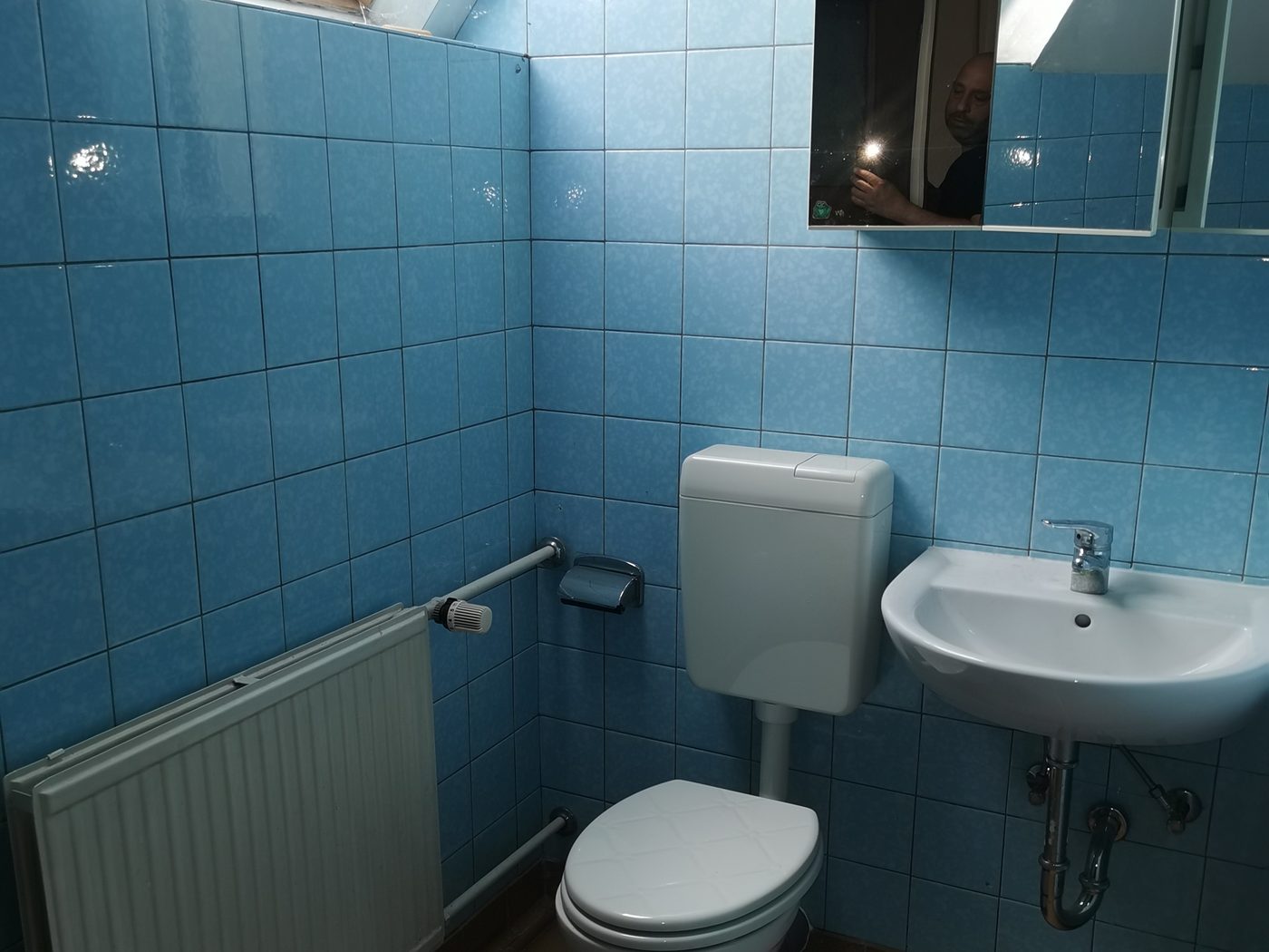 Kleines Bad unter der Dachschräge mit blauen Wandfliesen, WC, Waschbecken und Heizkörper