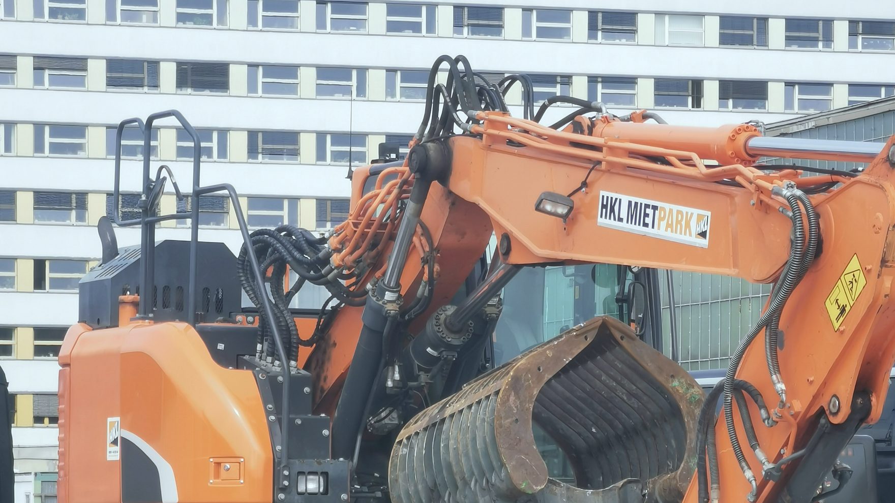 Kettenbagger mit Sortiergreifer auf dem Tieflader vor einem Berliner Plattenbau