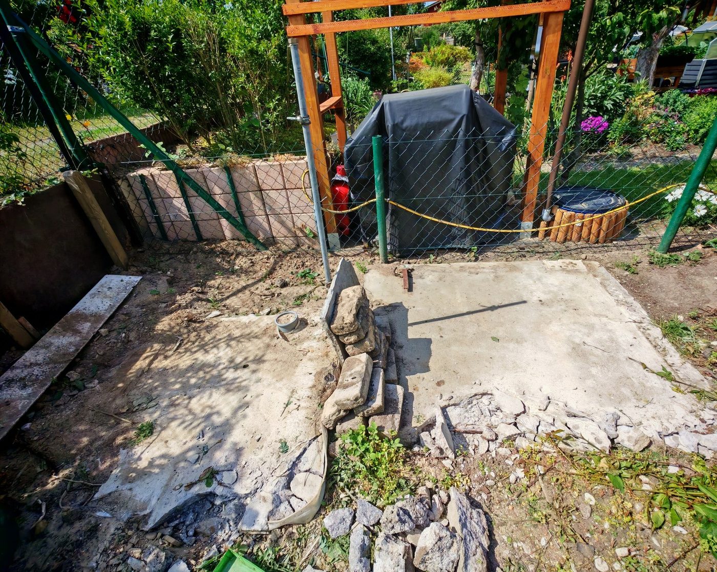 Betonplatte auf einer Kleingartenparzelle, am Rand erste Bruchstücke, dahinter ein Zaun