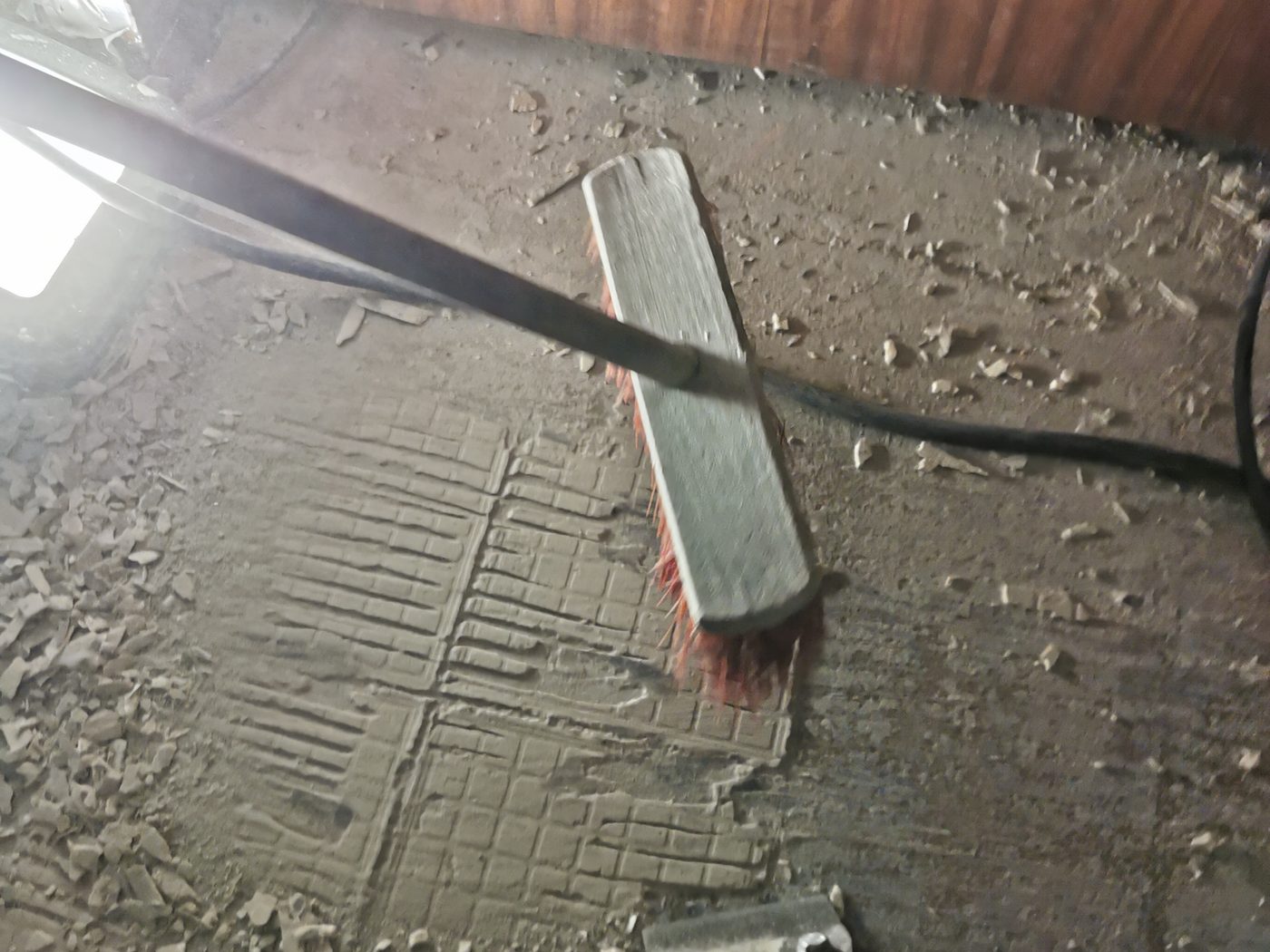 Stripper-Messer und Besen auf einem Estrich, von dem der verklebte Belag abgetragen ist