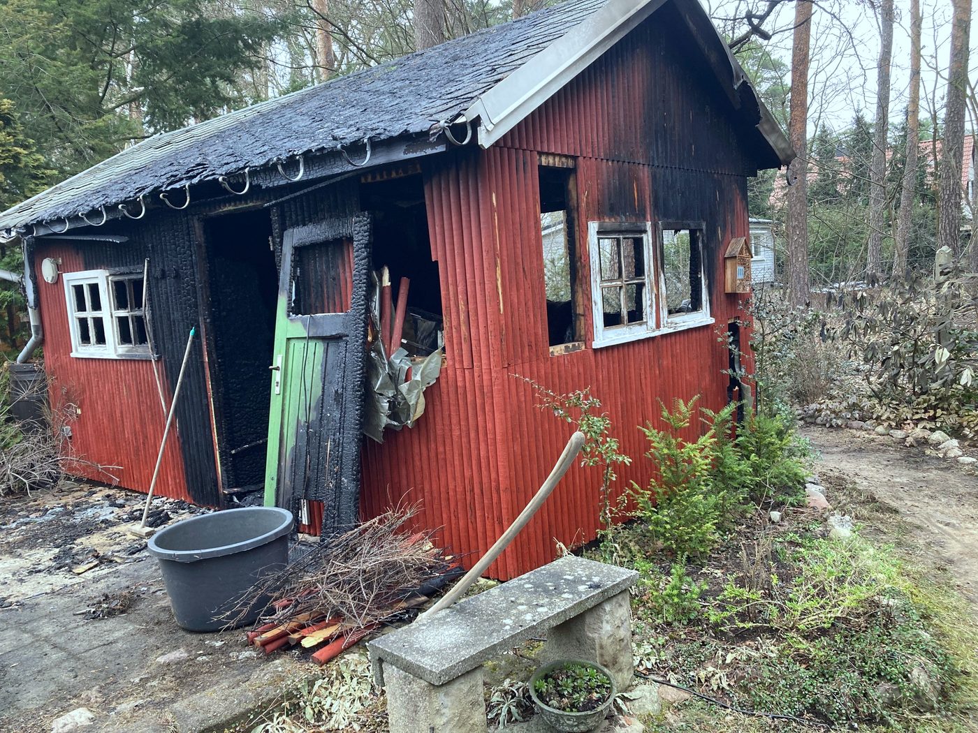 Ausgebranntes rotes Holzhaus im Kiefernwald, Dach und Wände verkohlt