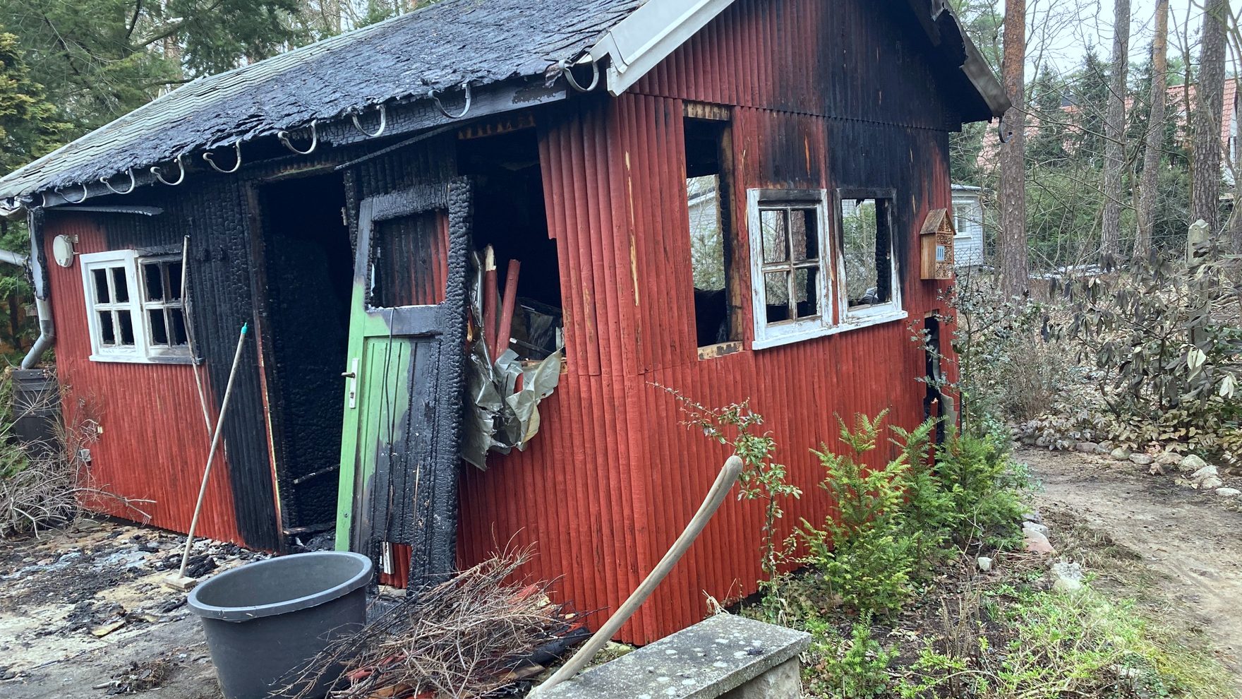 Ausgebranntes Holzhaus im Kiefernwald, Dach und Wände verkohlt
