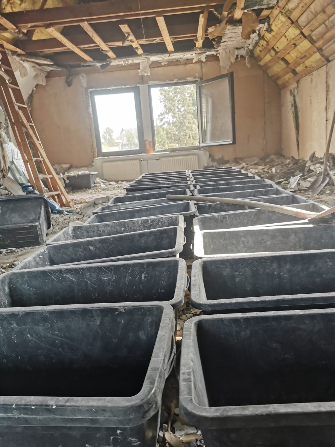Dachraum voller gefüllter Mörtelwannen mit sortiertem Bauschutt, bereit zum Abtransport