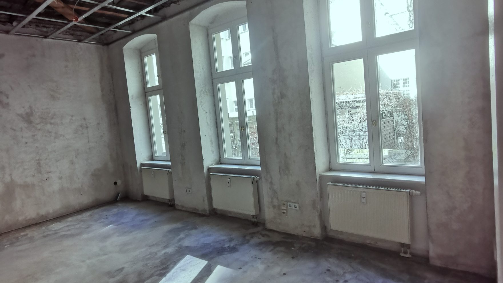 Entkernter Berliner Altbauraum mit drei Rundbogenfenstern und Sonnenlicht auf dem Estrich