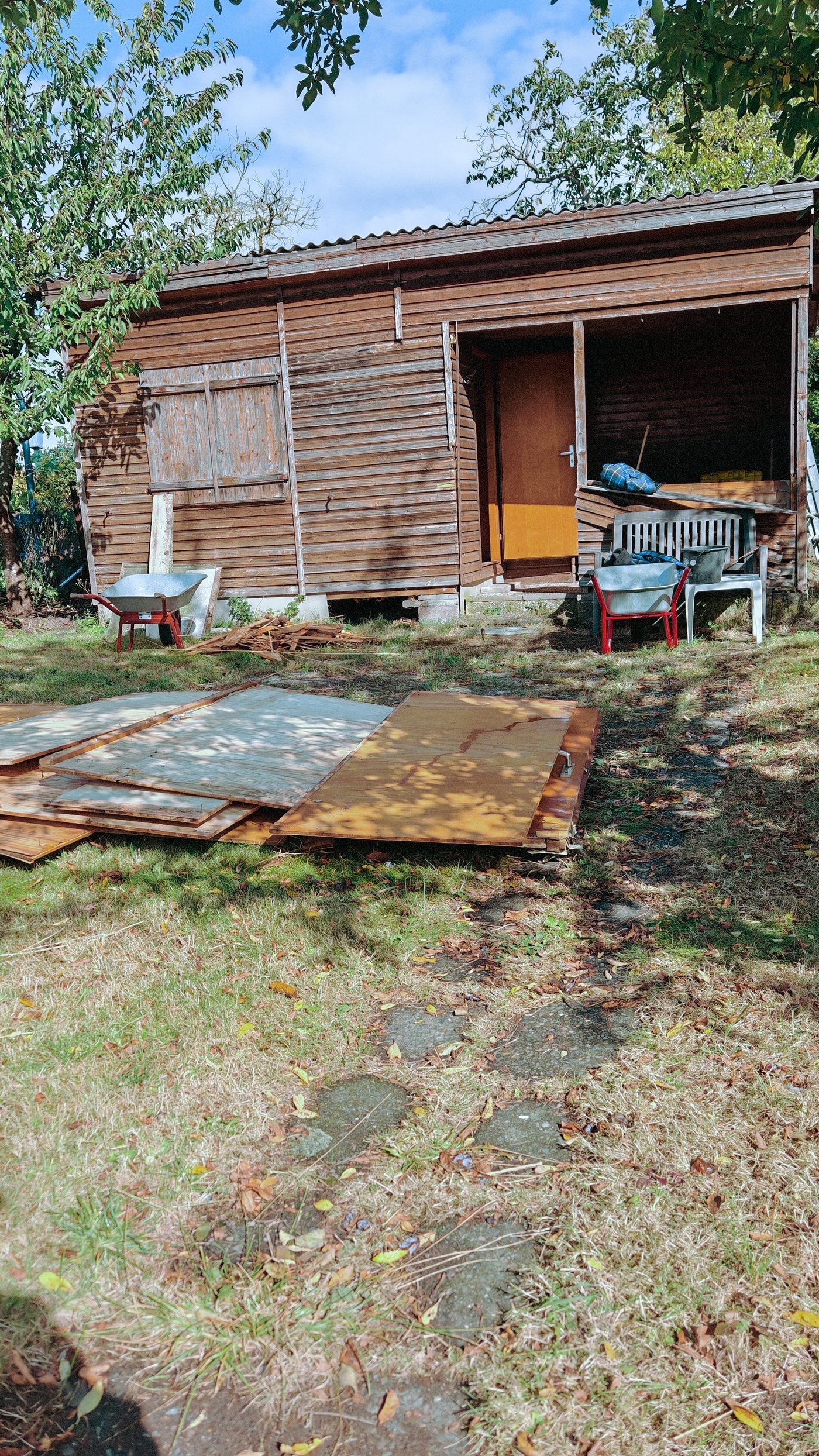 Gartenhaus aus Holz in einem Kleingarten, davor liegen die ersten abgenommenen Platten