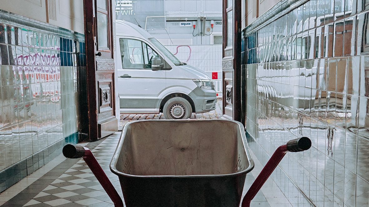 Berliner Hausflur mit historischen Wandfliesen und Schubkarre vor der offenen Haustür