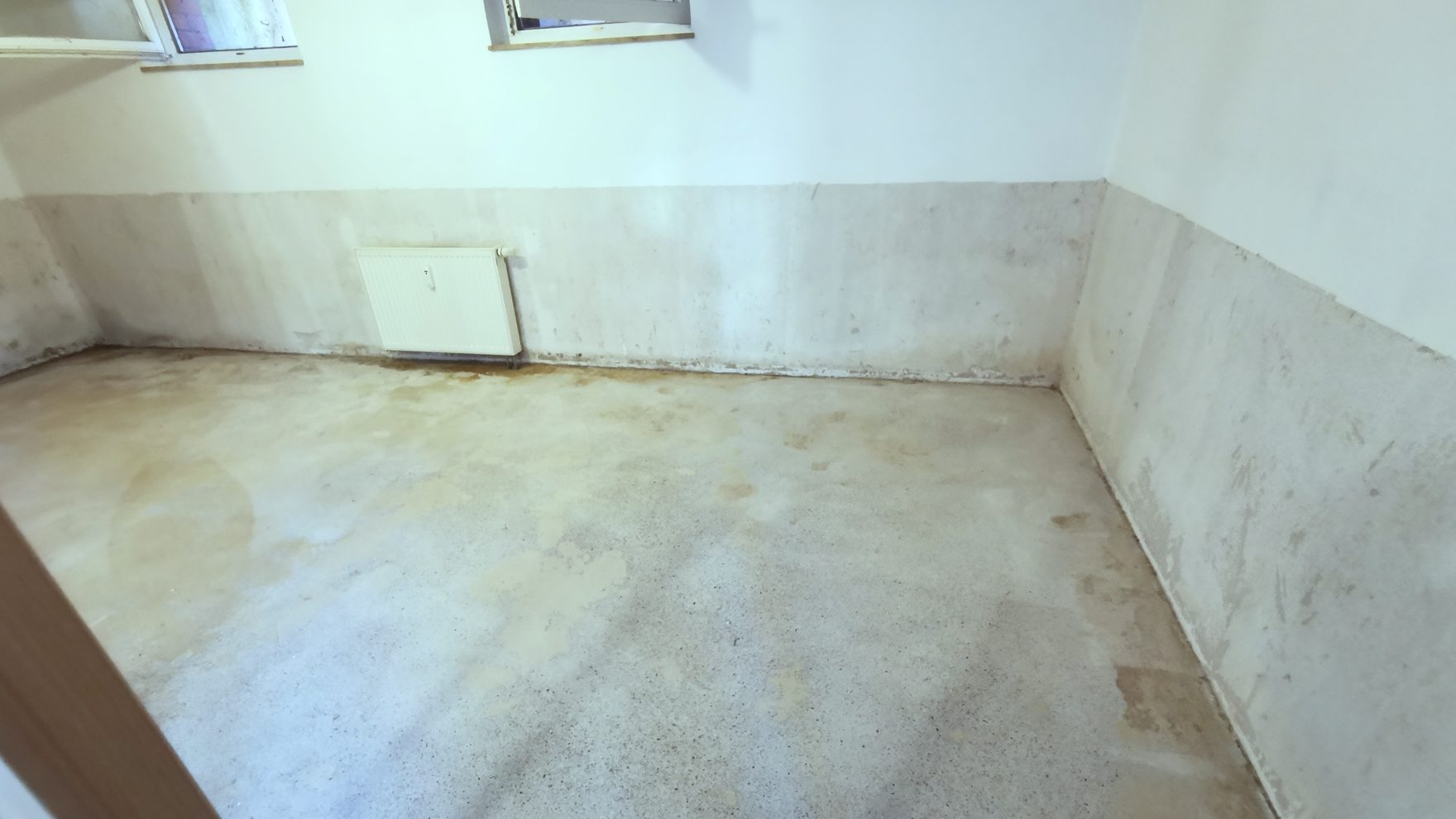 Kellerwand mit abgeschlagenem Sanierputz, der Heizkörper hängt unversehrt