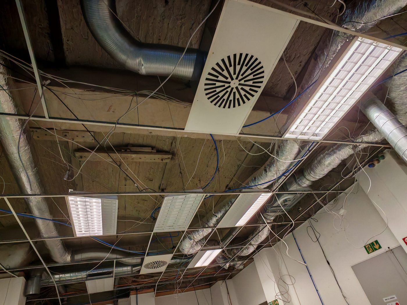 Geöffnete Rasterdecke mit Lüftungskanälen, Flexrohren und Kabelsträngen im Deckenhohlraum