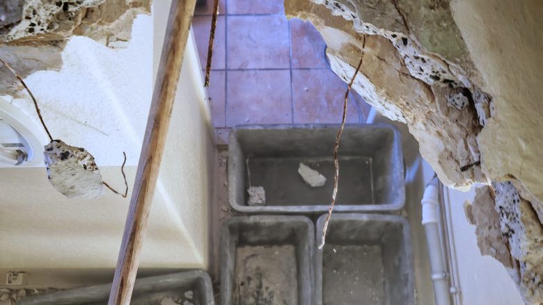 Geöffneter Wanddurchbruch im Altbau-Mauerwerk, Vorschlaghammer im Loch, Mörtelwannen darunter